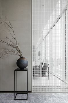 a black vase sitting on top of a table next to a tall white fenced wall