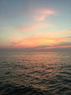 the sun is setting over the ocean as seen from a boat on the water in the distance