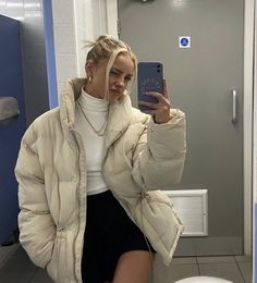 a woman is taking a selfie in the bathroom while wearing a puffy jacket