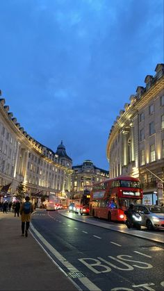 a city street filled with lots of traffic and tall buildings at night, along with people walking on the sidewalk