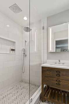 a bathroom with a walk in shower next to a sink and a wooden cabinet under the mirror