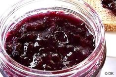 a glass jar filled with blueberry jam next to a piece of toasted bread