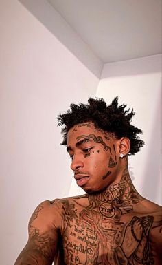 a man with tattoos on his face and chest is looking at the camera while standing in front of a white wall