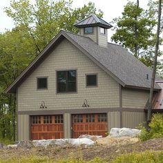 a two car garage sits in front of a wooded area with trees and rocks on the ground