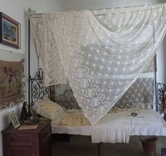 an old fashioned bed with white lace on it's canopy, in a bedroom