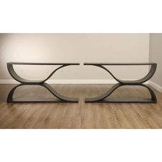 a modern console table with curved glass top and black metal frame, in an empty room