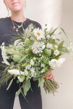 a woman holding a bouquet of white flowers and greenery in front of her face