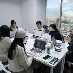 several people sitting around a table with laptops and papers on it in an office setting