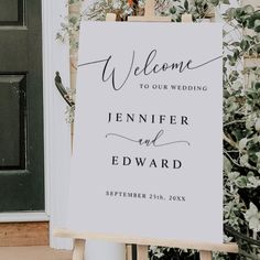 a welcome sign is standing in front of a door with greenery on the side