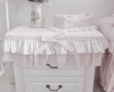 a white vase with flowers sitting on top of a table next to a bed and dresser