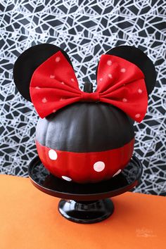 a mickey mouse pumpkin with a red bow on it sitting on top of a black plate