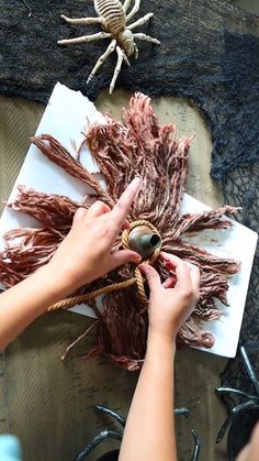 two hands are working on an art project with yarn and spiderweaves in the background