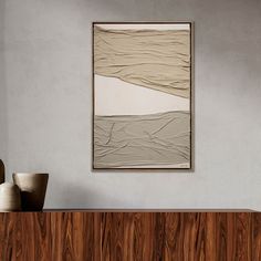 an abstract painting hangs on the wall above a wooden cabinet