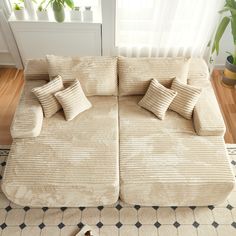 a couch with pillows on top of it in front of a rug and potted plant