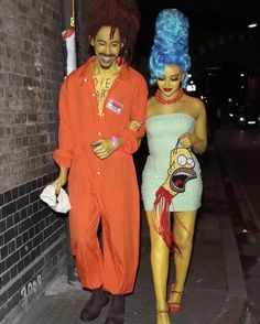 two people dressed in costumes walking down the street at night with one person wearing an orange wig