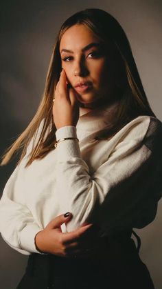 a woman posing with her hand on her chin and wearing a white sweater over her shoulders