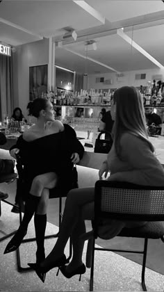 two women sitting in chairs talking to each other at a bar with bottles on the counter