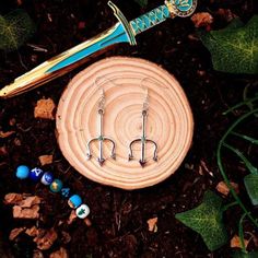 a pair of earrings sitting on top of a piece of wood next to some beads