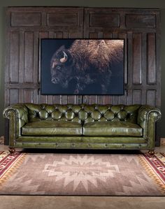 a green leather couch sitting in front of a wooden paneled wall with a bison painting on it