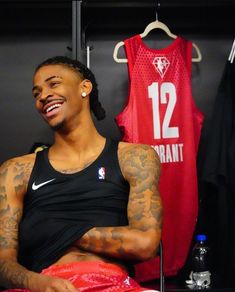 a man with tattoos sitting in front of a basketball jersey