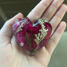 a hand holding a heart shaped piece of glass with flowers on it's side