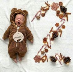 a baby in a bear costume laying next to christmas decorations and candy canes on a white blanket