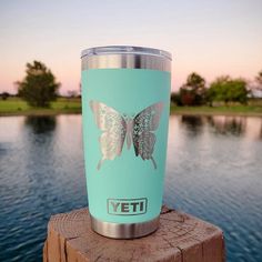 a blue yeti cup sitting on top of a wooden post next to a body of water