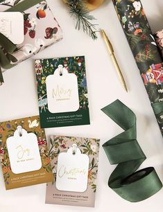 christmas gift tags on wrapping paper next to green ribbons and other holiday decorations with gold foil