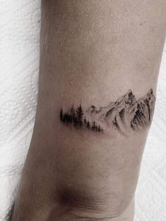 a tattoo on the arm of a person with mountains and trees in the back ground