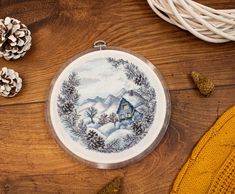 a cross stitch ornament on a wooden table with pine cones