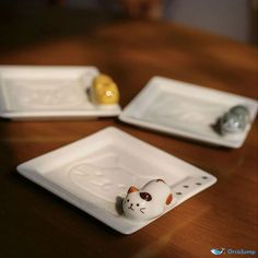 two white plates with cats on them sitting on top of a wooden table next to each other