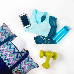 the contents of a gym bag laid out on a white surface, including water bottle, dumbbells and cell phone