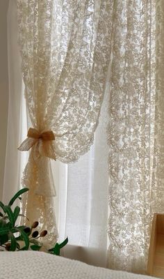 a white bed sitting next to a window covered in sheer curtains and a bow tie