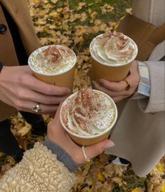 Three friends are in a circle and holding up cups of hot coffee with whipped cream on top. Fall Drinks