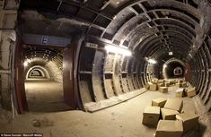 an underground tunnel with cardboard boxes on the floor and light at the end in the middle