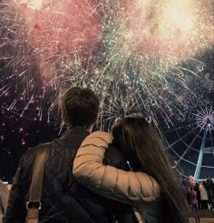 a man and woman looking at fireworks in the sky with their arms around each other