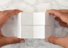 two hands holding white boxes on a marble surface