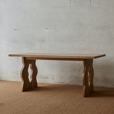 a wooden table sitting on top of a carpeted floor next to a white wall