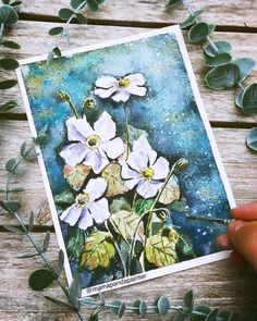 a person is holding up a card with flowers on it and leaves surrounding it,