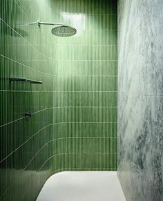 a green tiled bathroom with a white toilet and shower head mounted to the side of the wall