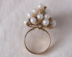 "This over the top, eye catching cocktail ring has to be worn to be appreciated. The ring features a cluster of 17 lustrous white pearls, accented by yellow gold nuggets and genuine gemstones arranged through out the design. The setting sits high on top of the finger but the band is flat and comfortable to wear. This retro era ring truly embodies the \"big and bold\" look of that time period and will definitely be a conversation starter on your hand! GEMSTONES: Genuine Sapphires: 2 @ 1.75mm, Gen Heirloom White Cluster Ring, Fine Jewelry Pearl Ring With 17 Jewels For Wedding, White Cluster Ring For Formal Occasions, White Cluster Ring With 17 Jewels, White Pear-shaped Cluster Ring For Formal Occasions, Pear-shaped White Cluster Ring For Formal Occasions, Formal White Cluster Ring, White Cluster Pearl Ring For Wedding, Formal Multi-stone Pearl Ring In Fine Jewelry Style