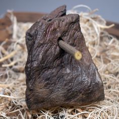 a piece of rock sitting on top of some dried up grass with a knife sticking out of it