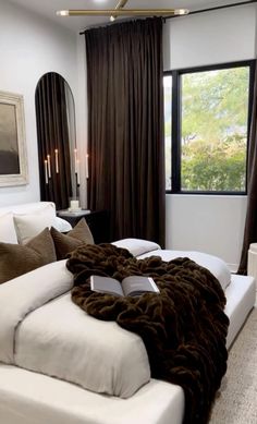 a large white bed sitting in a bedroom next to a window with brown drapes