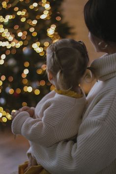 a woman holding a small child in front of a christmas tree with lights on it