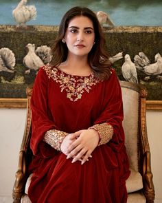 a woman sitting in a chair wearing a red dress with gold embroidery on the sleeves