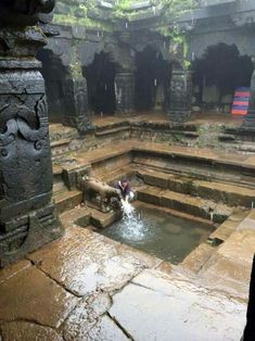 a man standing next to a small pool in a stone building with carvings on the walls