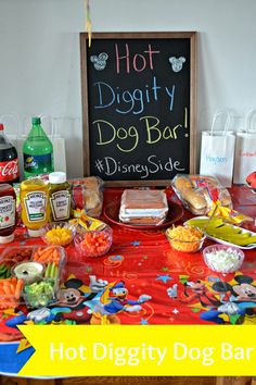 a hot dog bar is set up with condiments and snacks on the table