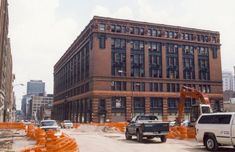 an old brick building is being renovated with construction equipment in the foreground and cars parked on the street behind it