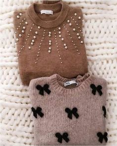 two sweaters with bows on them are sitting on a white knitted surface and one is