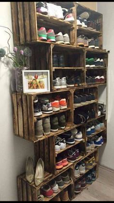 a wooden shoe rack filled with lots of pairs of shoes next to a white wall